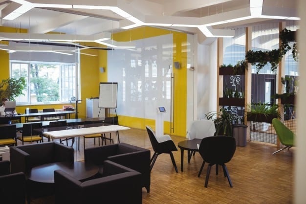 A modern open office plan with black furniture, yellow walls, and wooden flooring. 